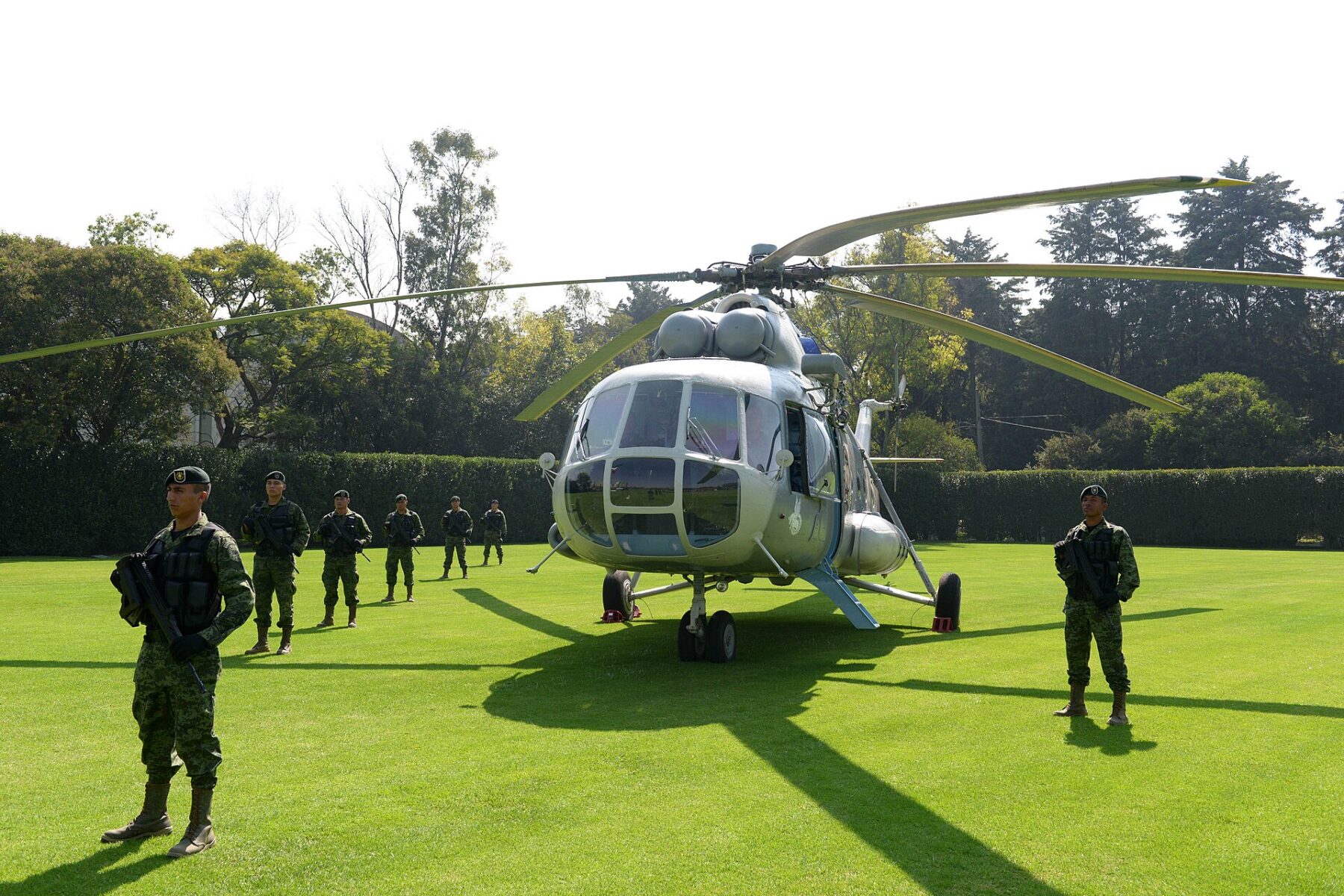 Mexican soldiers in camouflage stand guard around a grey Mi-17 helicopter on a lawn in Mexico City