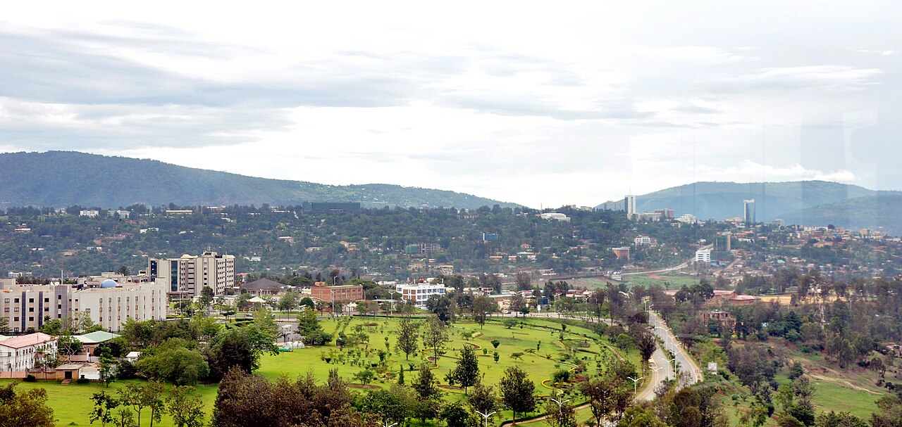 Green hillsides and a landscaped park in Kigali, with office towers of the downtown district on the horizon at right.