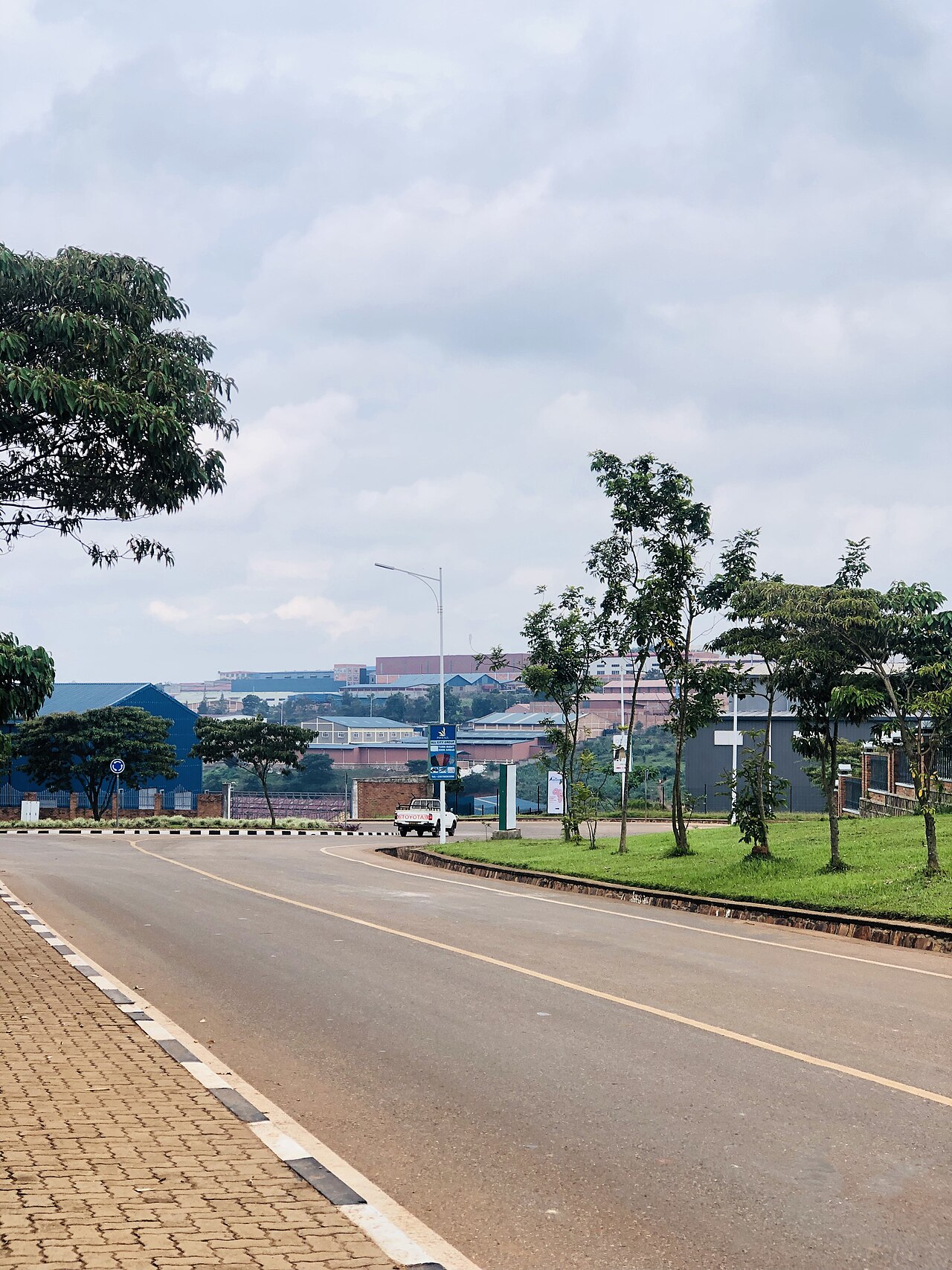 A paved road curving past warehouses and factory sheds on the industrial site in Kigali, under a cloudy sky.