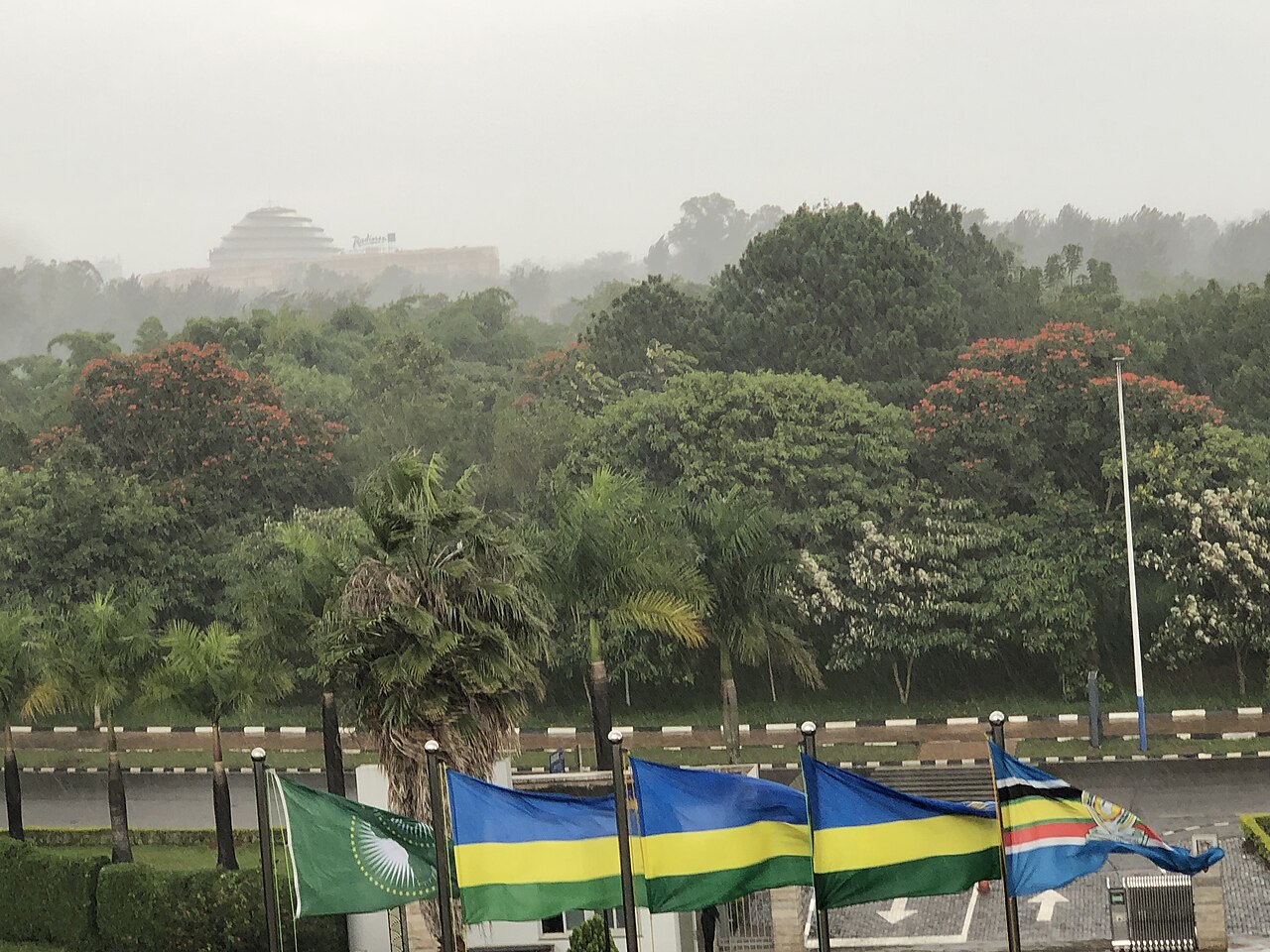 Rwandan, African Union and East African Community flags in the rain in Kigali, with the convention centre dome behind trees