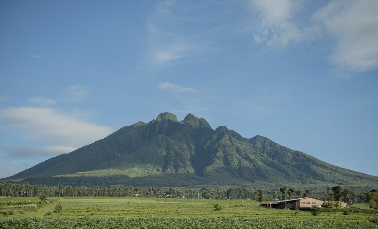 Mount Sabyinyo, a green volcano in northern Rwanda, rising above farmland under a blue sky