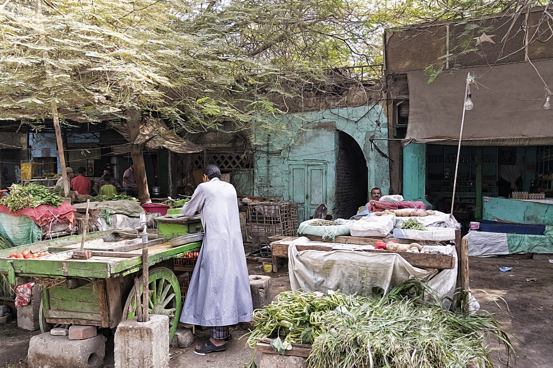 Vegetable stalls and wooden carts at a street market, with a man in a long robe standing at a cart