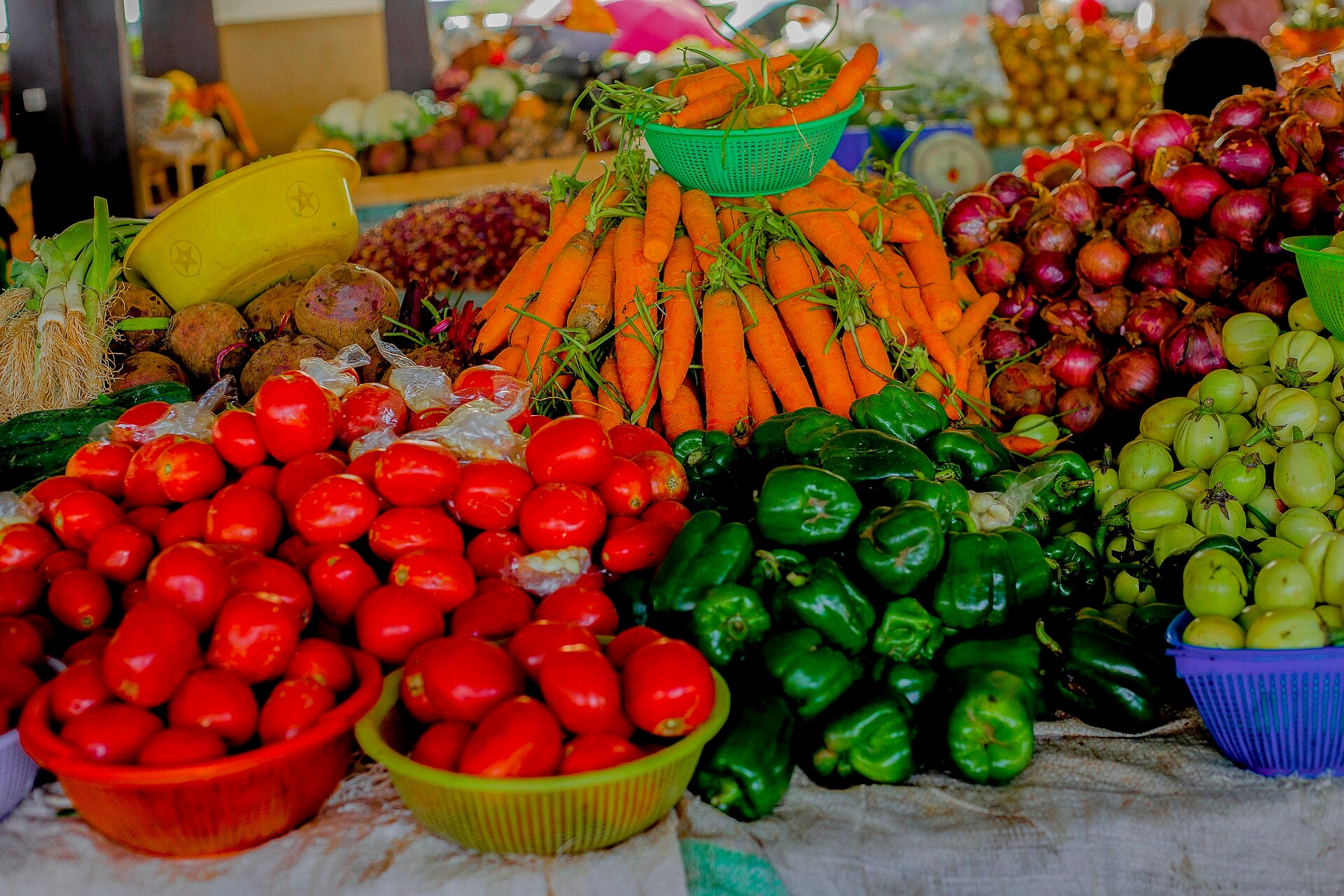 Baskets of tomatoes, green peppers, carrots, red onions and garden eggs on a market table