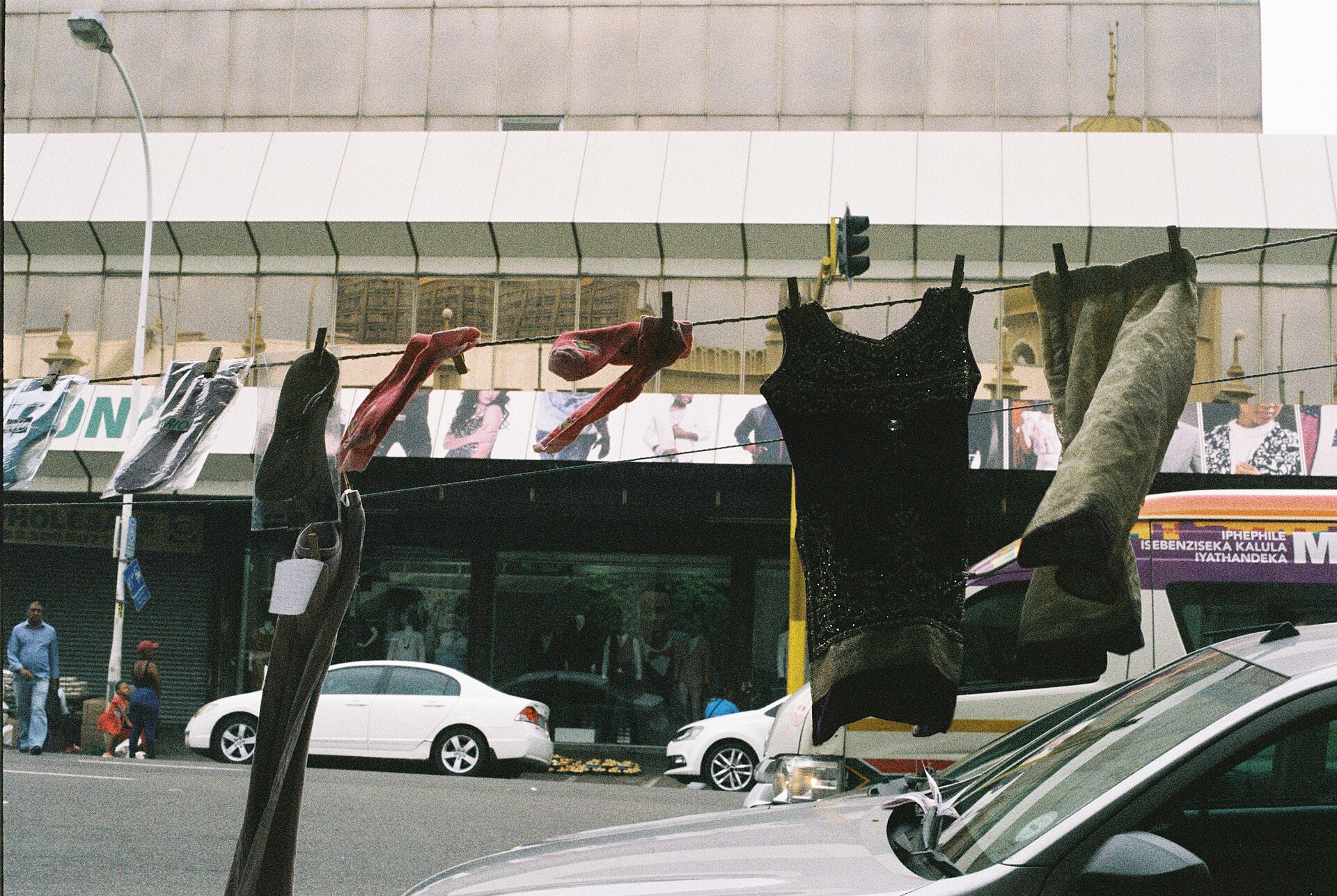 Clothes hung for sale on a line across a street in central Durban, with shops and parked cars behind