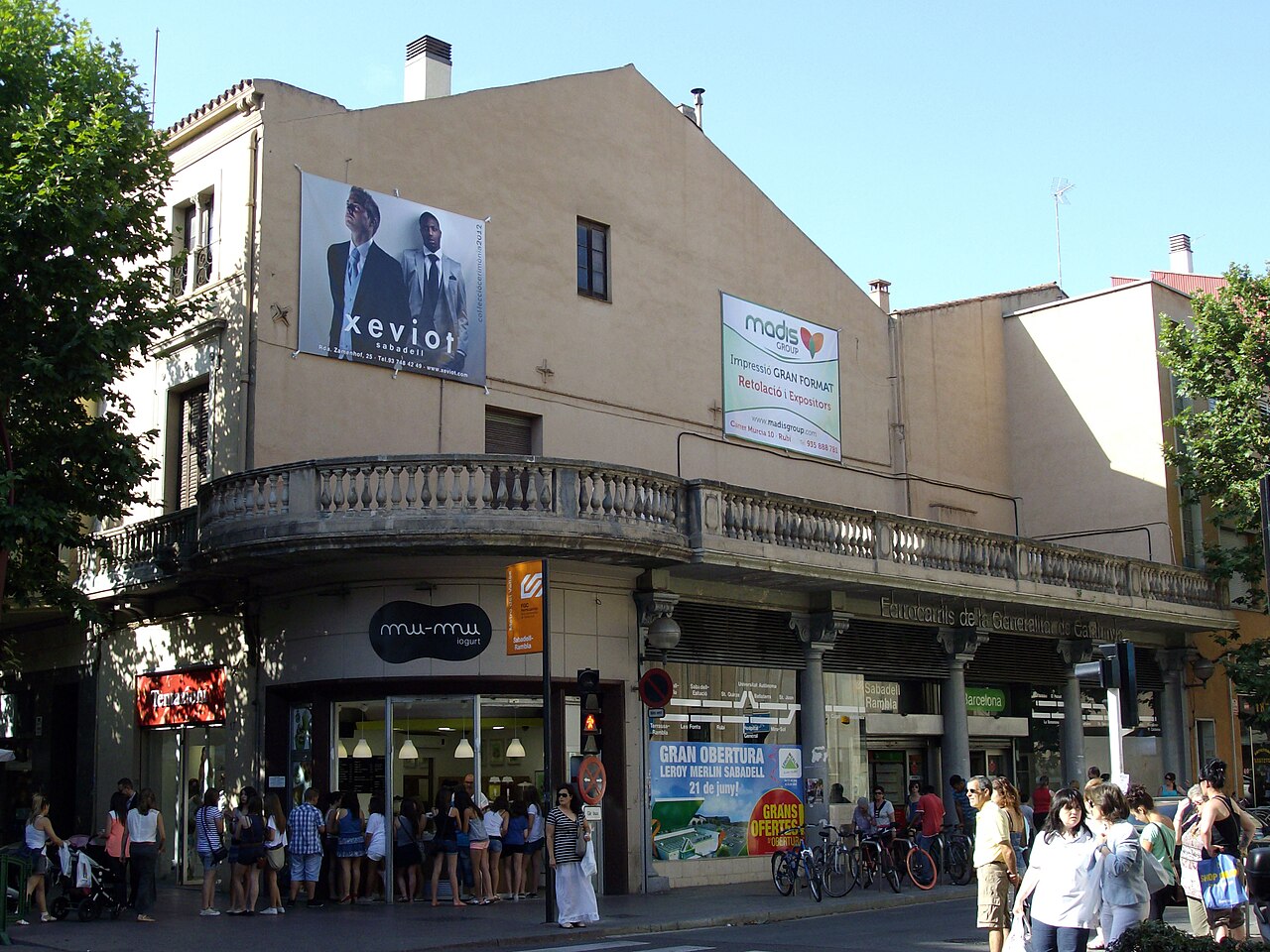 The Sabadell-Rambla commuter rail station building, with a balustraded balcony and shoppers on the street corner