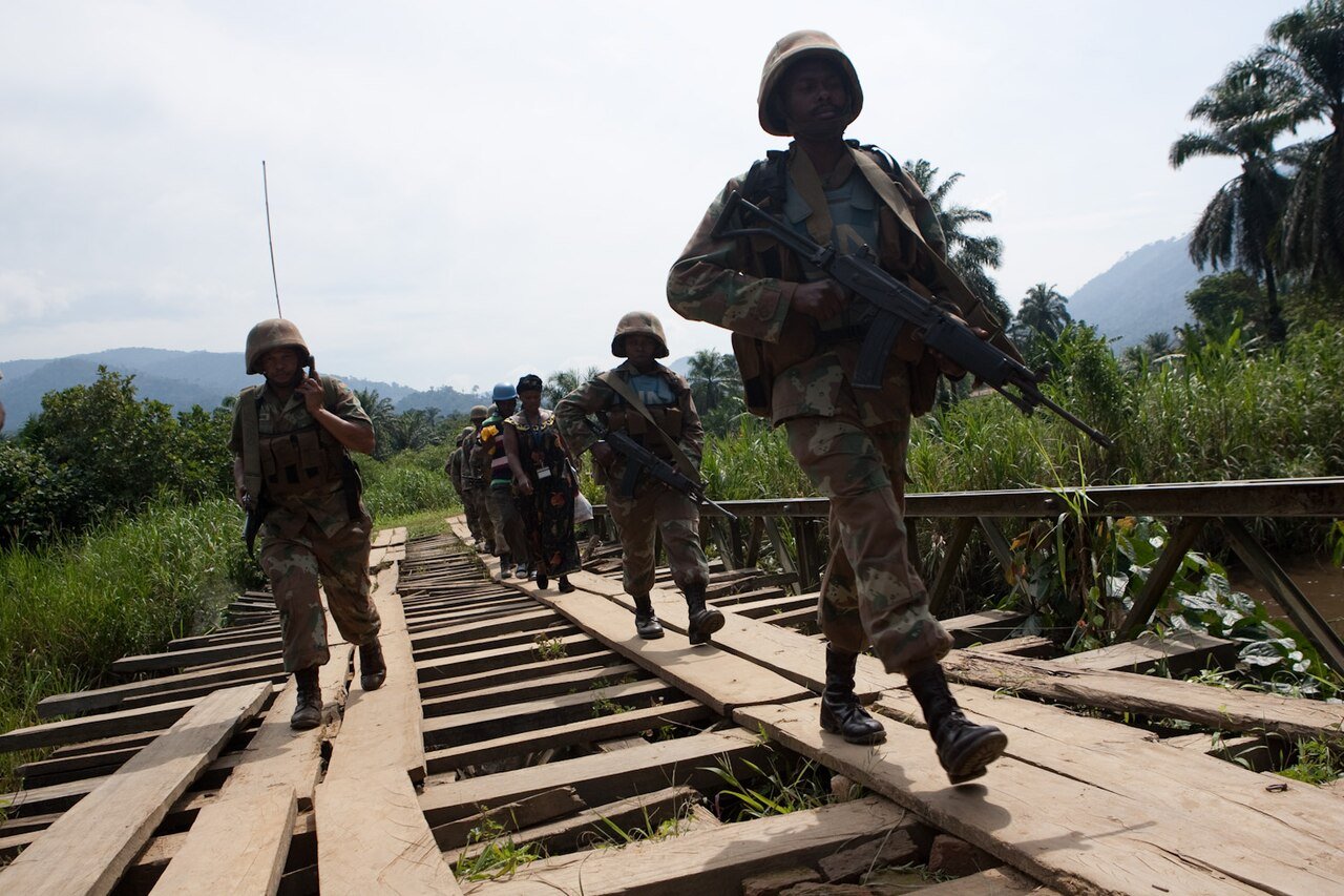 South African soldiers in helmets and body armour on patrol crossing a wooden bridge near Pinga in North Kivu, eastern DR Congo