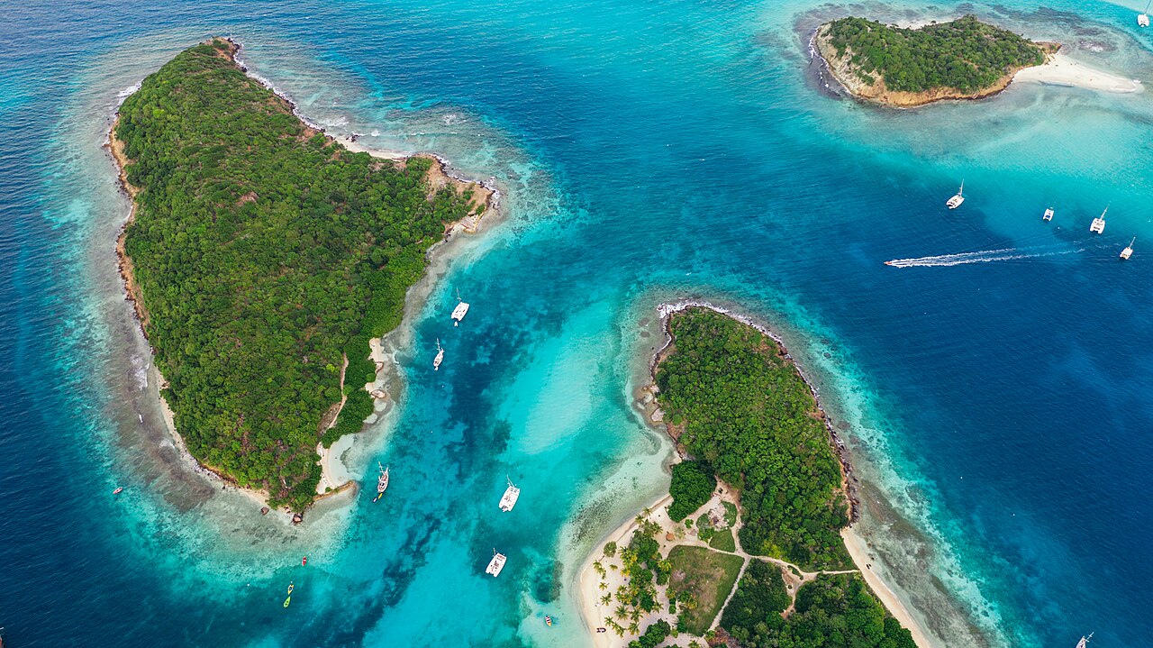Aerial view of small green islands ringed by turquoise water with sailboats anchored among the Tobago Cays in the Grenadines