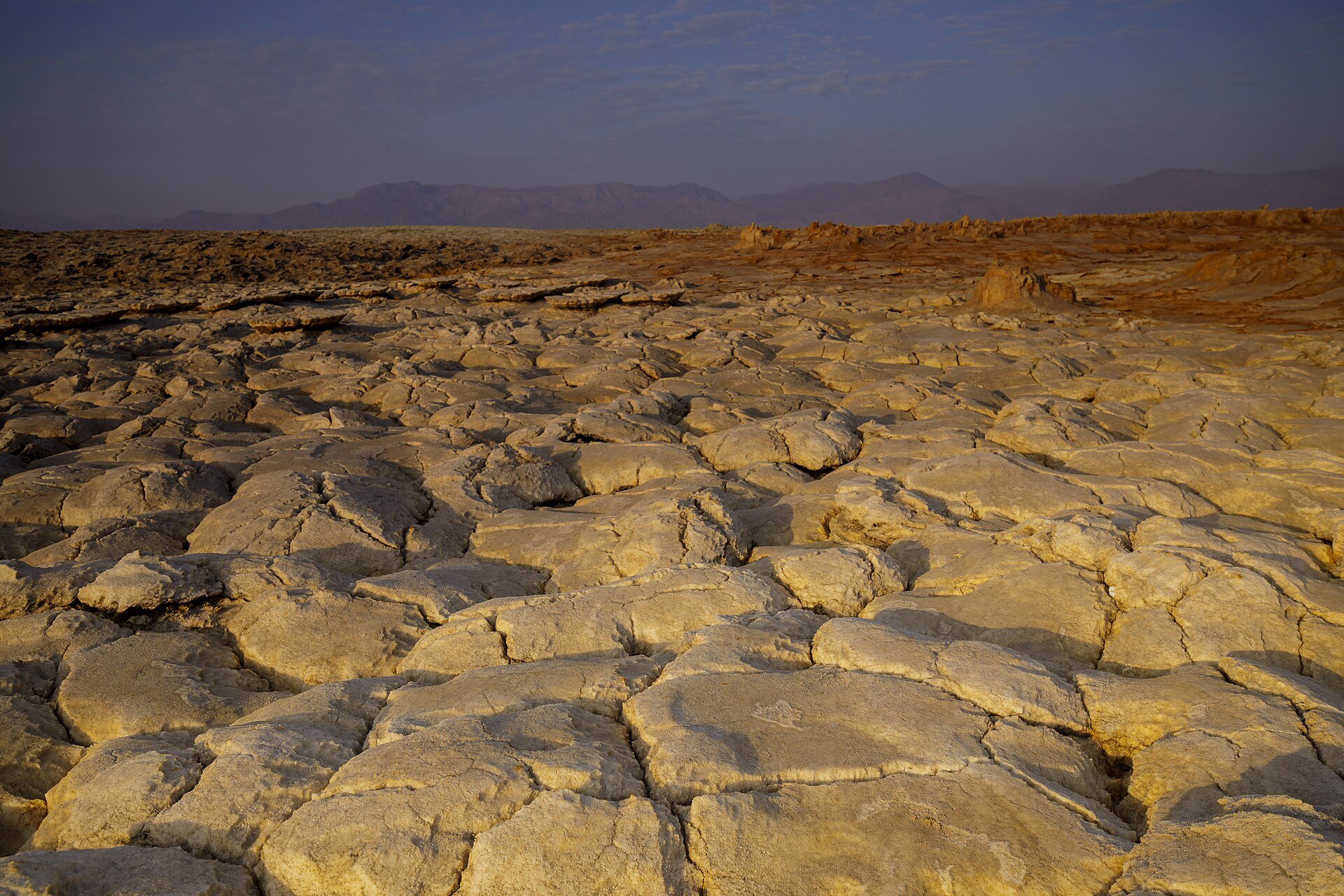 Cracked salt crust and mineral flats of the Danakil Depression in Ethiopia's Afar Region under a dusk sky with mountains behind