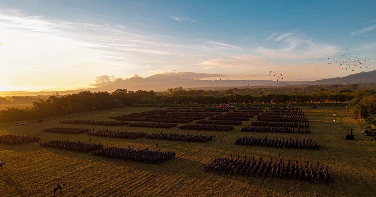 Rows of Salvadoran soldiers in formation on a field at sunrise with volcanoes behind