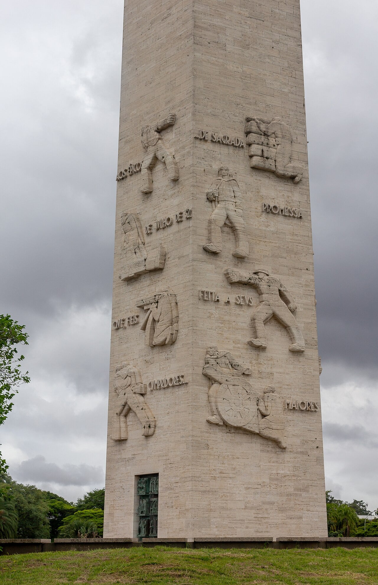 Close view of the stone obelisk at Ibirapuera in São Paulo, with carved relief figures of soldiers and Portuguese lettering on its face.