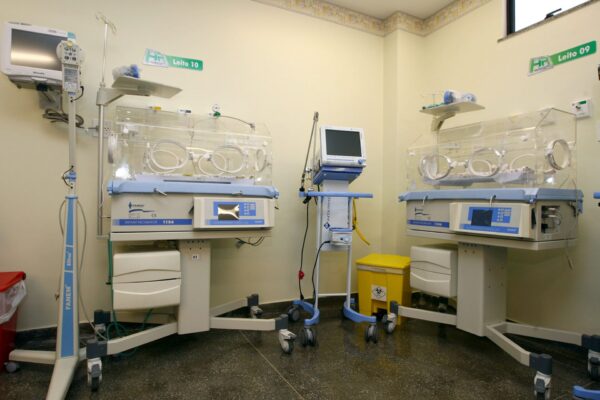 Two empty infant incubators with monitors and bed number labels in a neonatal intensive care room with yellow walls