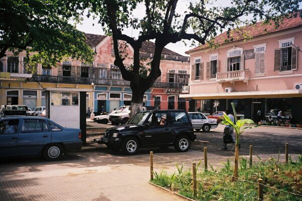 Cars parked on a central square in Sao Tome with pink colonial-era buildings behind
