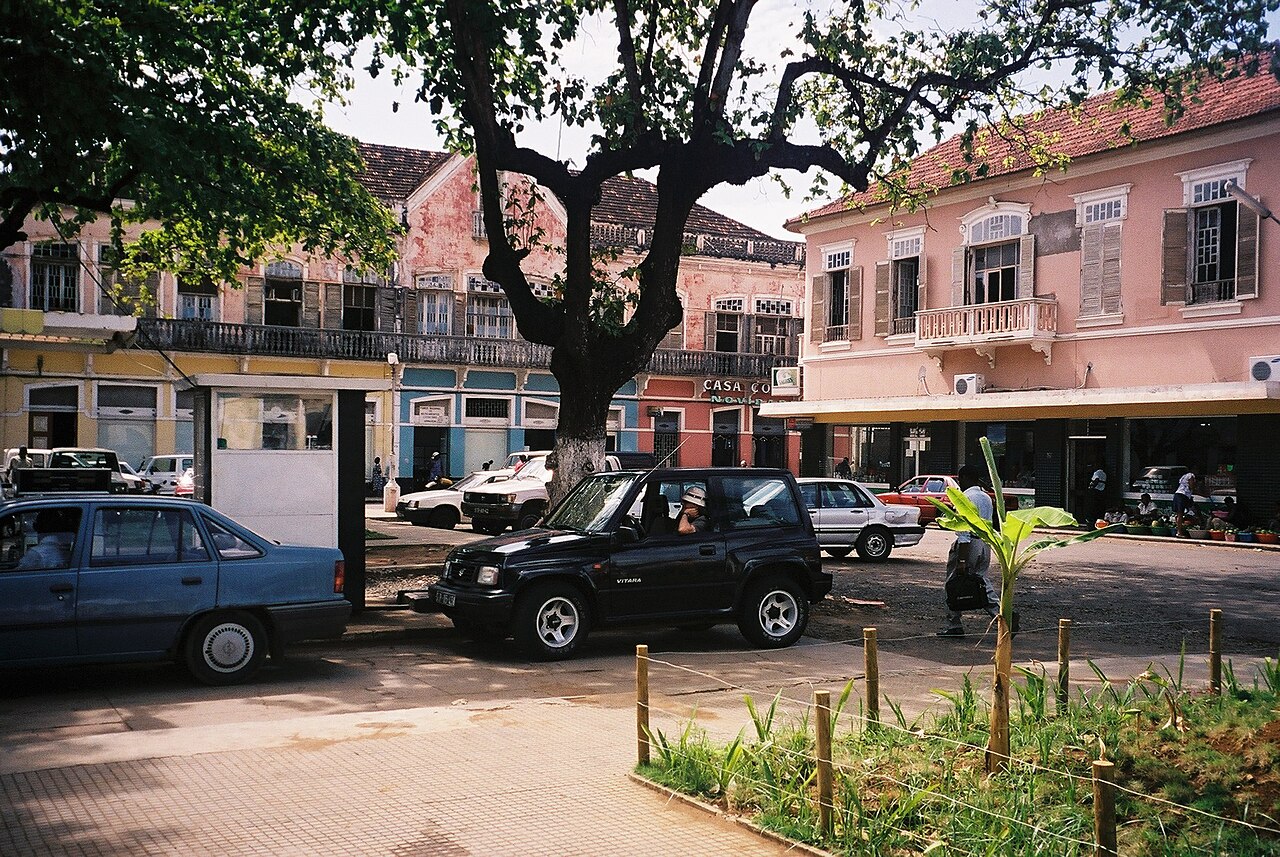 Cars parked on a central square in Sao Tome with pink colonial-era buildings behind