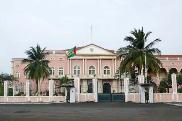 Pink presidential palace in São Tomé with the national flag, palm trees and guard boxes at the gate