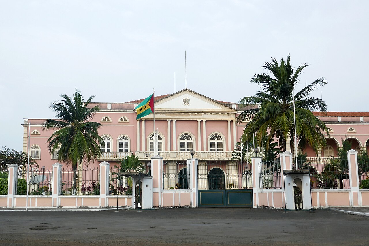 Pink presidential palace in São Tomé with the national flag, palm trees and guard boxes at the gate