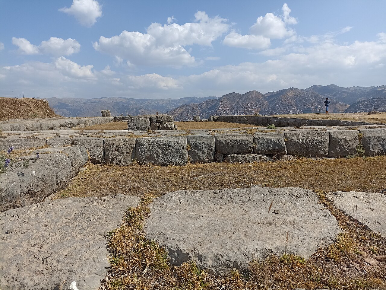 Stone terraces and open ground at the Saqsaywaman archaeological park, with Andean hills behind, Cusco, Peru.