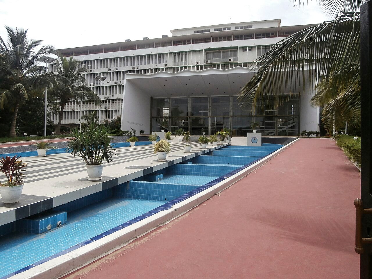The National Assembly building in Dakar, a white modern block behind a tiled blue water feature and palm trees