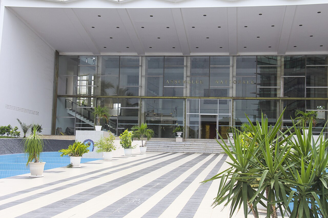 The glass entrance hall of the National Assembly in Dakar, with the words Assemblée Nationale above the doors and a tiled forecourt with potted plants