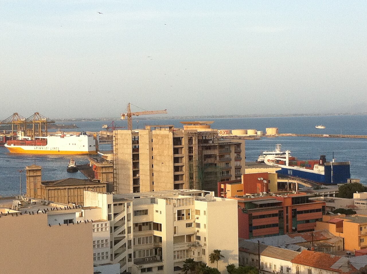 Cargo ships, container cranes and fuel storage tanks at the port of Dakar behind city buildings
