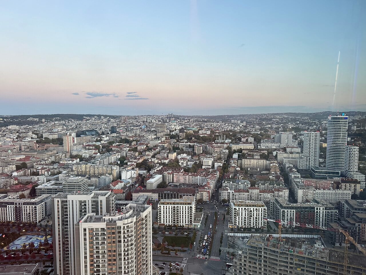 View over central Belgrade, Serbia, from a high tower at dusk, with apartment blocks, a glass tower and the dome of a cathedral on the horizon