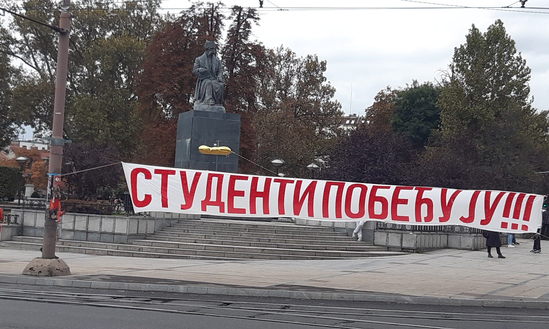 Red banner reading Students Win in Cyrillic in front of the Vuk Karadžić monument in Belgrade