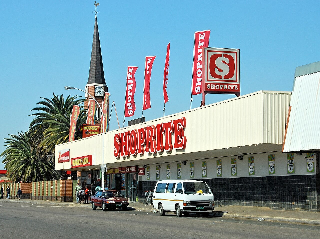 Shoprite supermarket with red signs and flags beside a church spire in Zeerust, South Africa