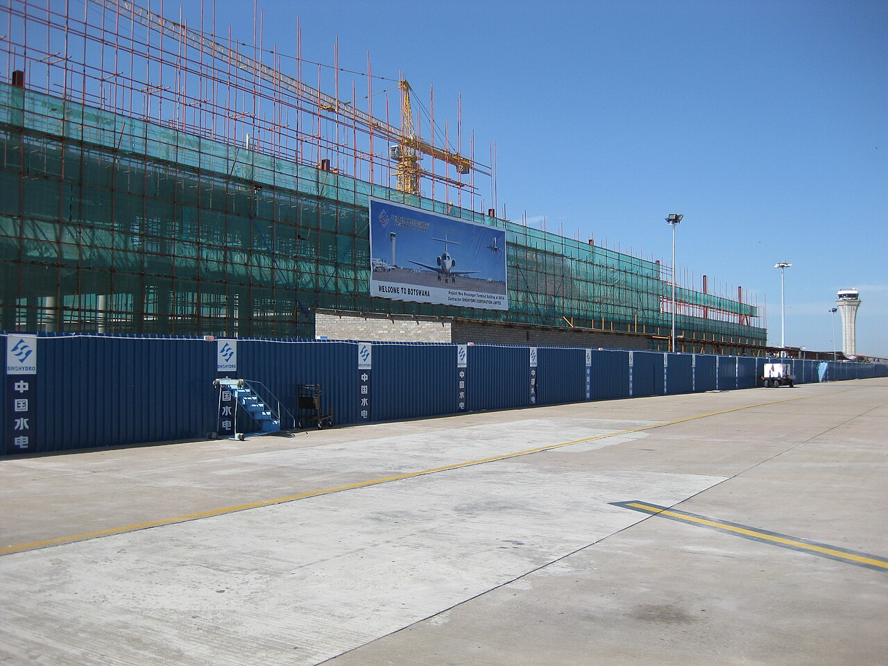 The terminal building of Sir Seretse Khama International Airport near Gaborone under construction, with scaffolding, a crane, the control tower and an apron