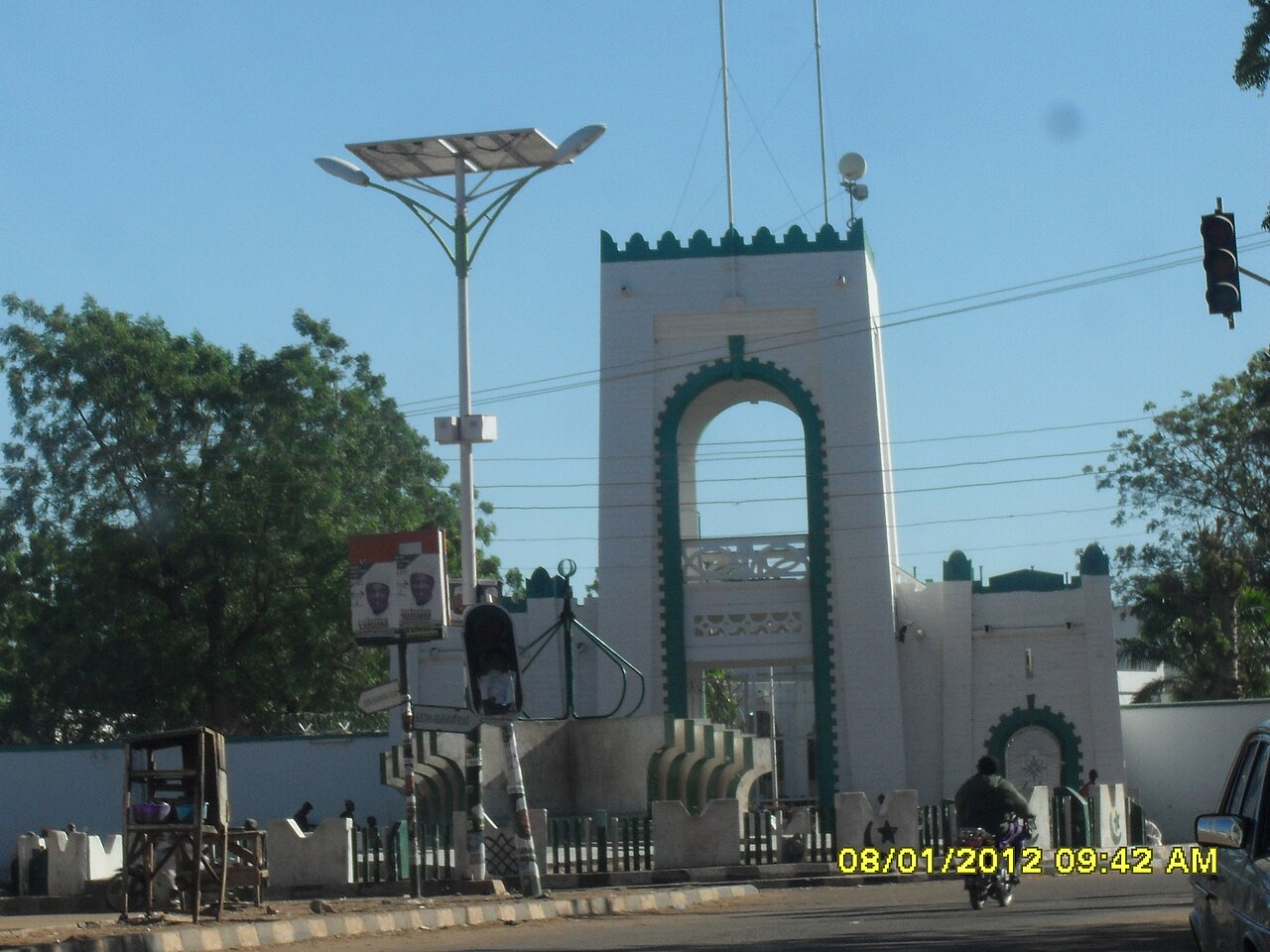 The white and green gateway of the Sultan of Sokoto's palace in Sokoto city, with a street lamp and a motorcycle in front