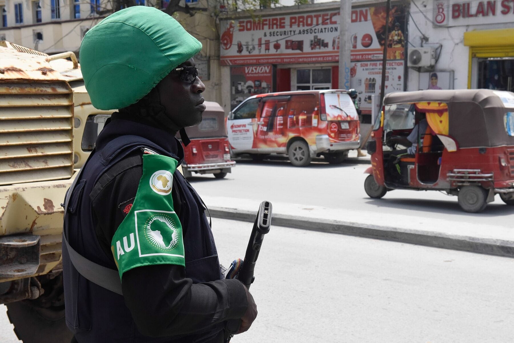 African Union police officer on a street in Mogadishu, Somalia, with an armoured vehicle and tuk-tuks behind