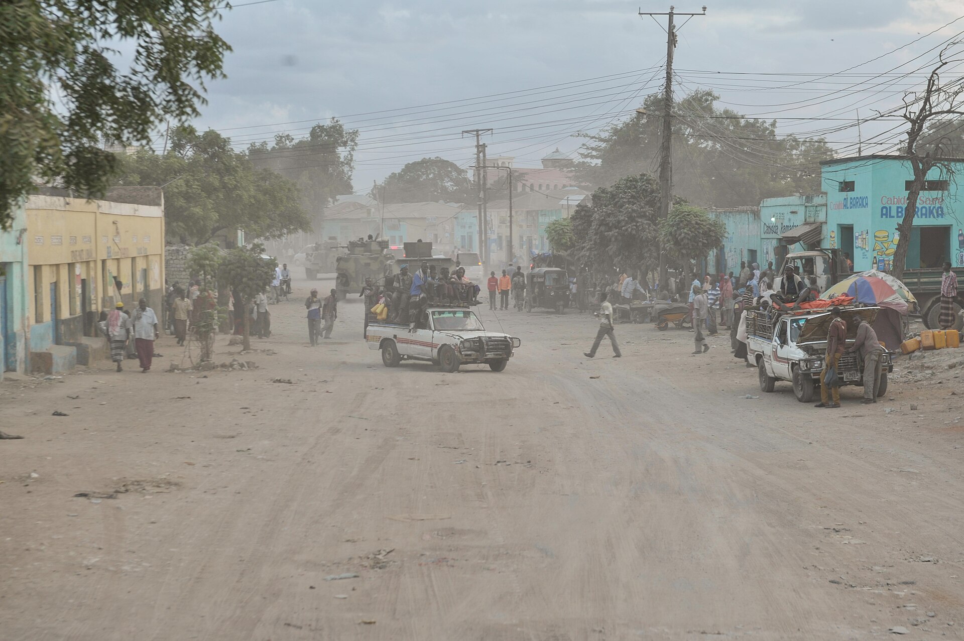 Dusty main street in downtown Baidoa, Somalia, with pickup trucks, pedestrians and painted shopfronts at dusk