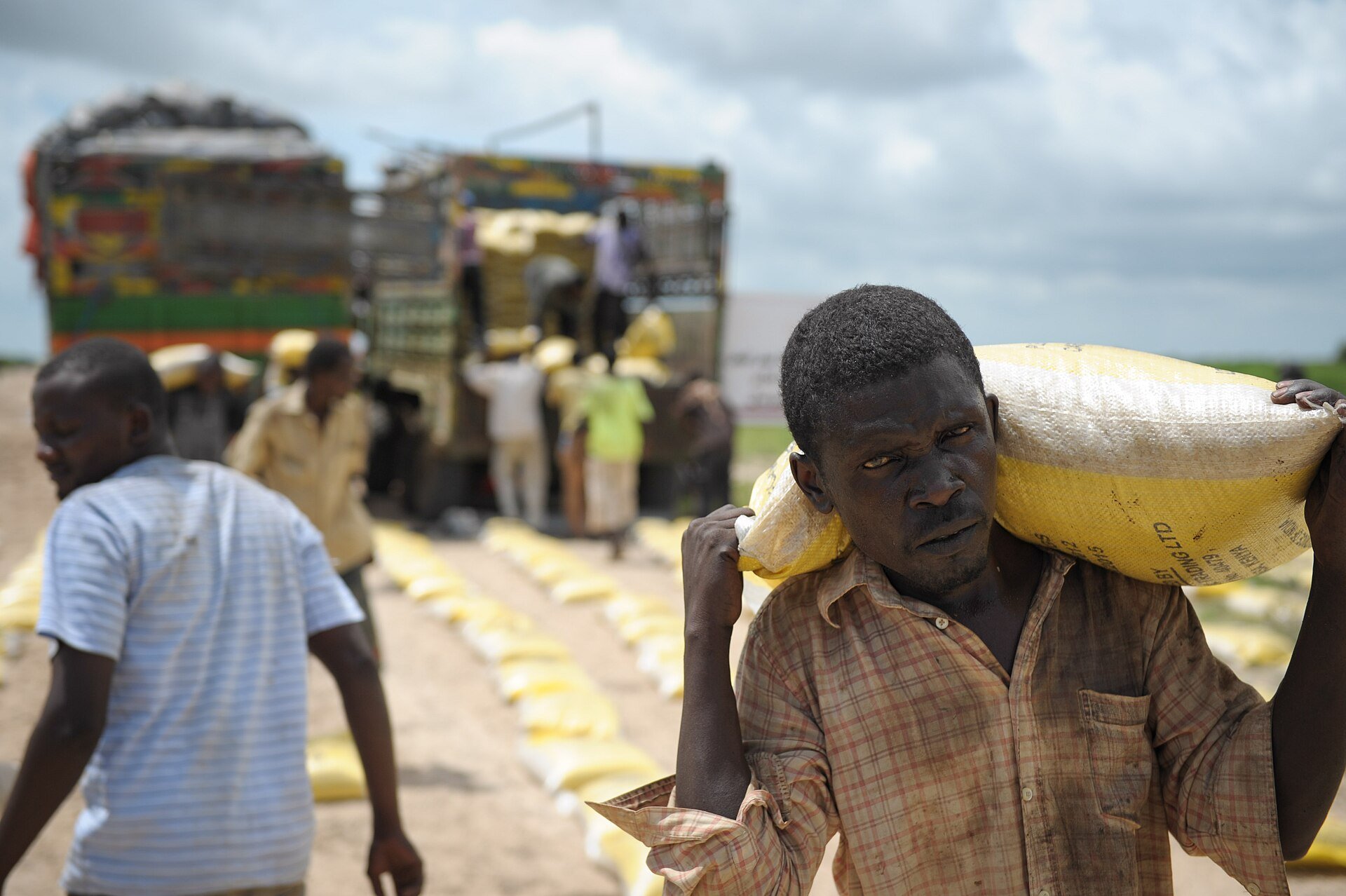 A man carries a sack of food aid past parked trucks for displaced people in Jowhar, Somalia