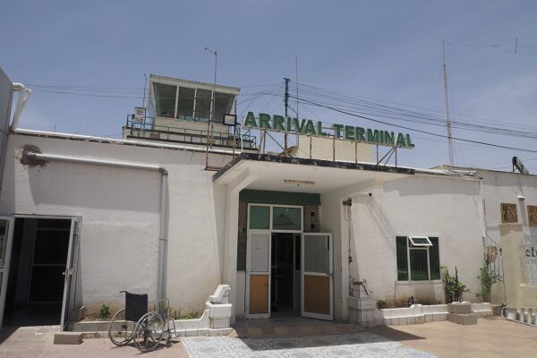 Arrival terminal of the airport in Hargeisa, Somaliland, with a control tower, a green sign and an empty wheelchair outside