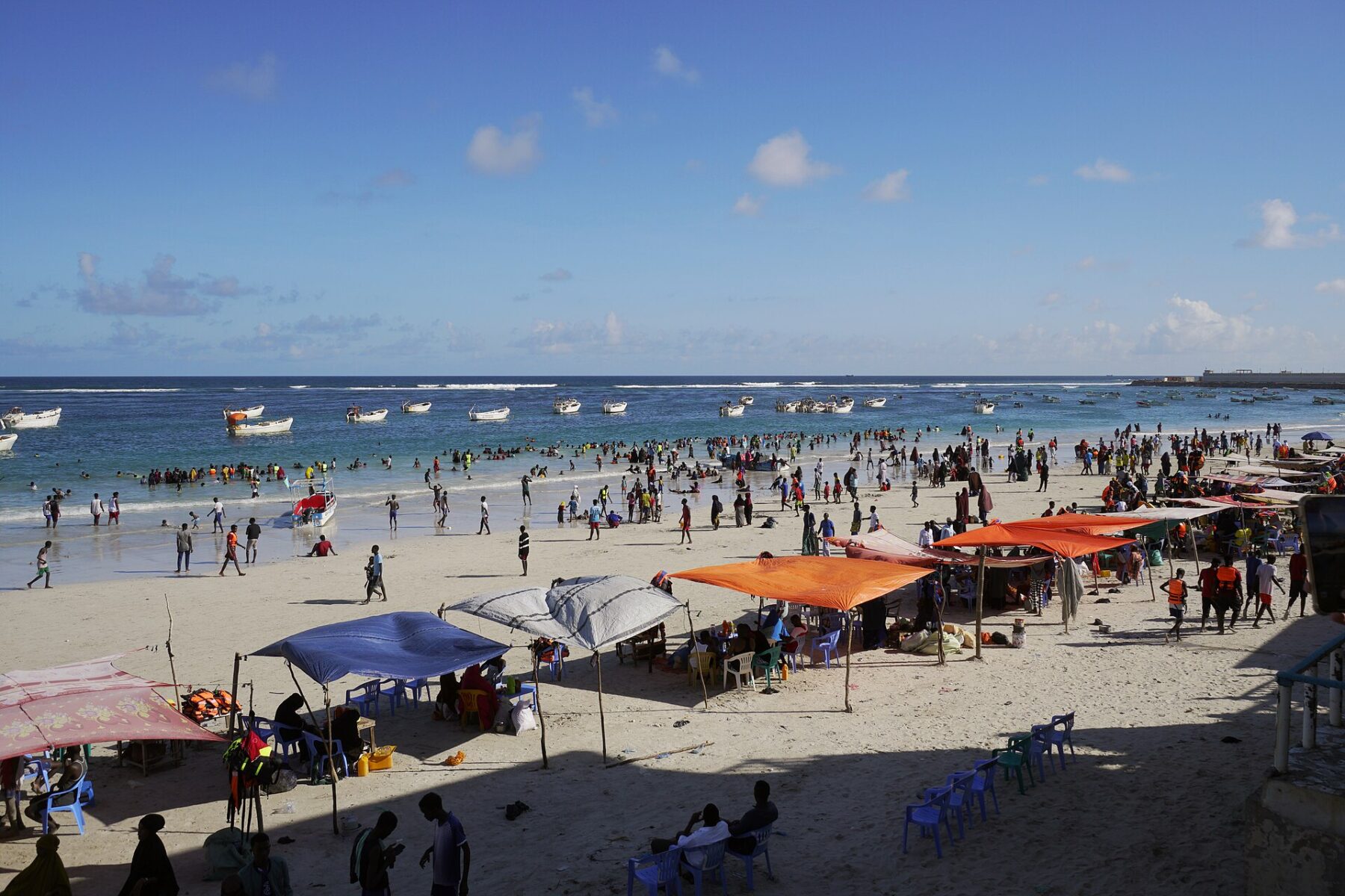 Lido Beach in Mogadishu, Somalia, with swimmers, shade tents and boats offshore
