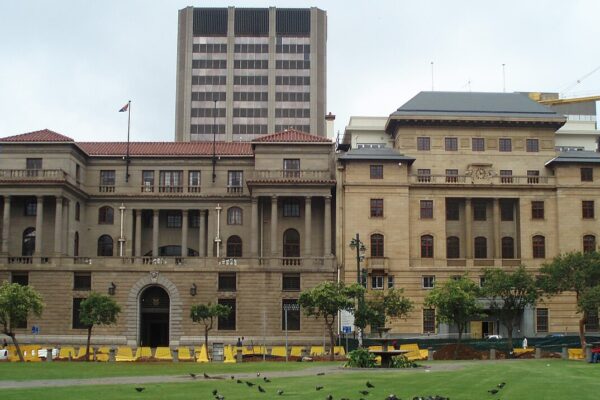 The sandstone Old Reserve Bank and Mutual Building on Church Square in Pretoria, with an office tower behind it and pigeons on the lawn in front