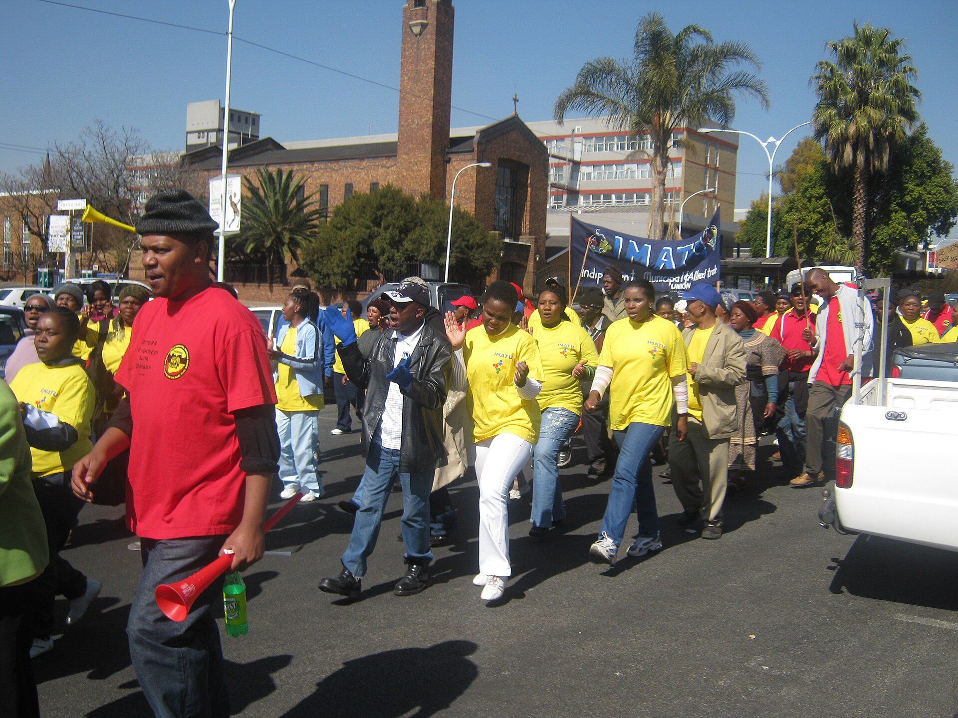 Striking municipal workers in red and yellow union shirts march along a street in Boksburg, South Africa