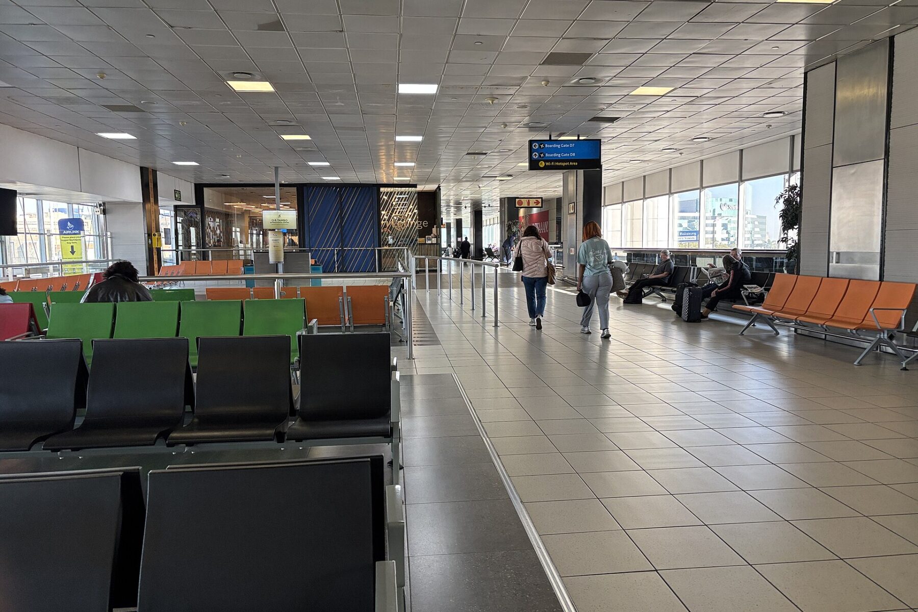 Passengers walk past rows of seats in a waiting area at OR Tambo International Airport in Johannesburg