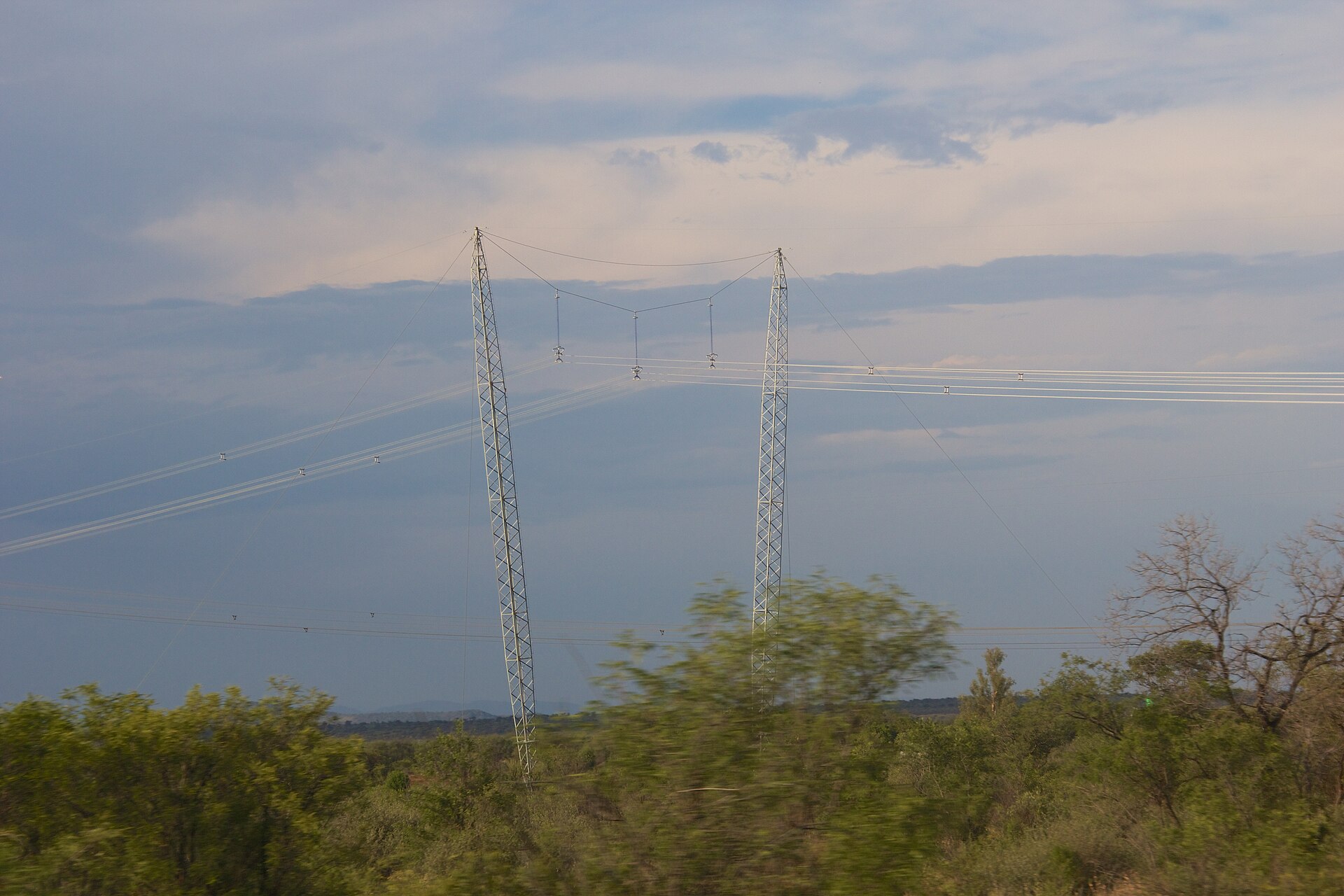 High-voltage power line towers and cables above green bush in South Africa
