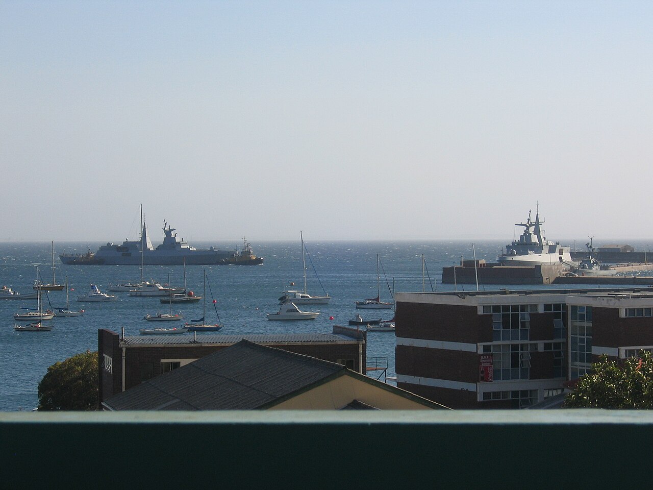 Grey South African Navy frigates in the bay at Simon's Town, with moored yachts and harbour buildings in the foreground