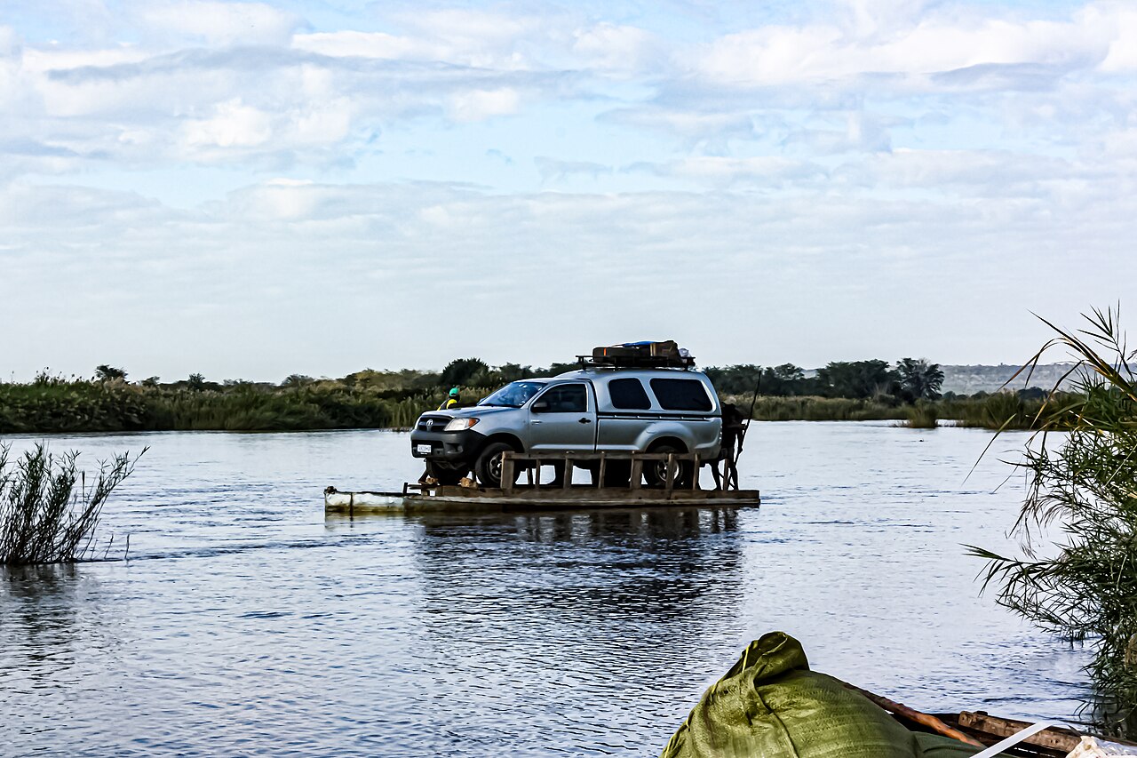 A silver pickup truck carried across the wide Limpopo River on a small wooden ferry raft, with reeds on both banks