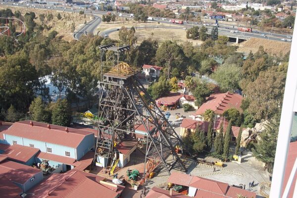 Steel headgear of an old gold mine shaft at Gold Reef City in Johannesburg, seen from above with red-roofed buildings and a highway behind
