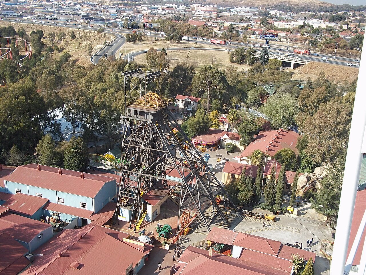 Steel headgear of an old gold mine shaft at Gold Reef City in Johannesburg, seen from above with red-roofed buildings and a highway behind