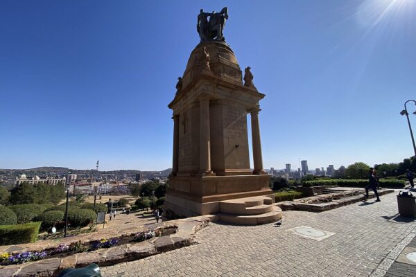 Sandstone war memorial with a bronze horse and rider on the grounds of the Union Buildings in Pretoria, with the city skyline behind it