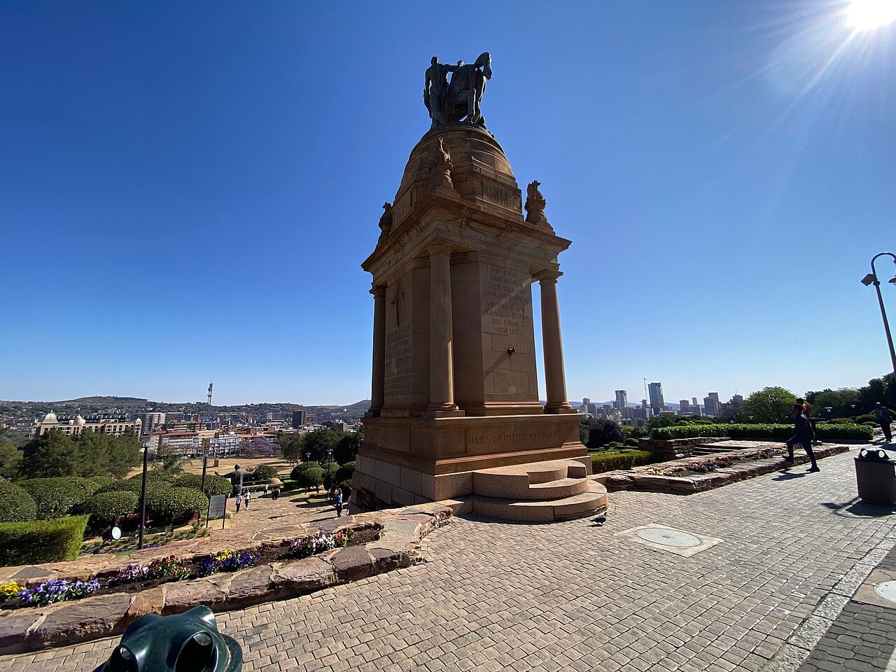 Sandstone war memorial with a bronze horse and rider on the grounds of the Union Buildings in Pretoria, with the city skyline behind it