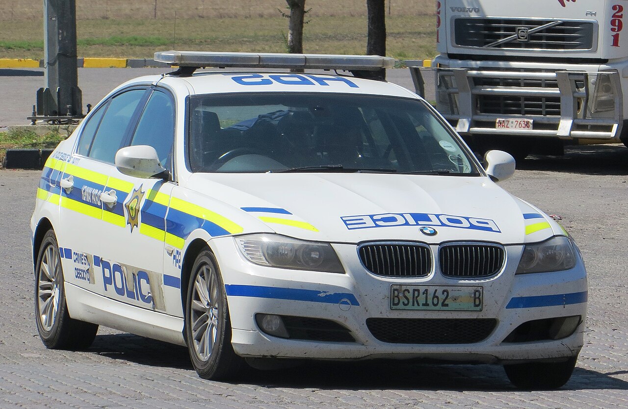 White BMW police car with blue and yellow stripes and a light bar, parked on a paved lot