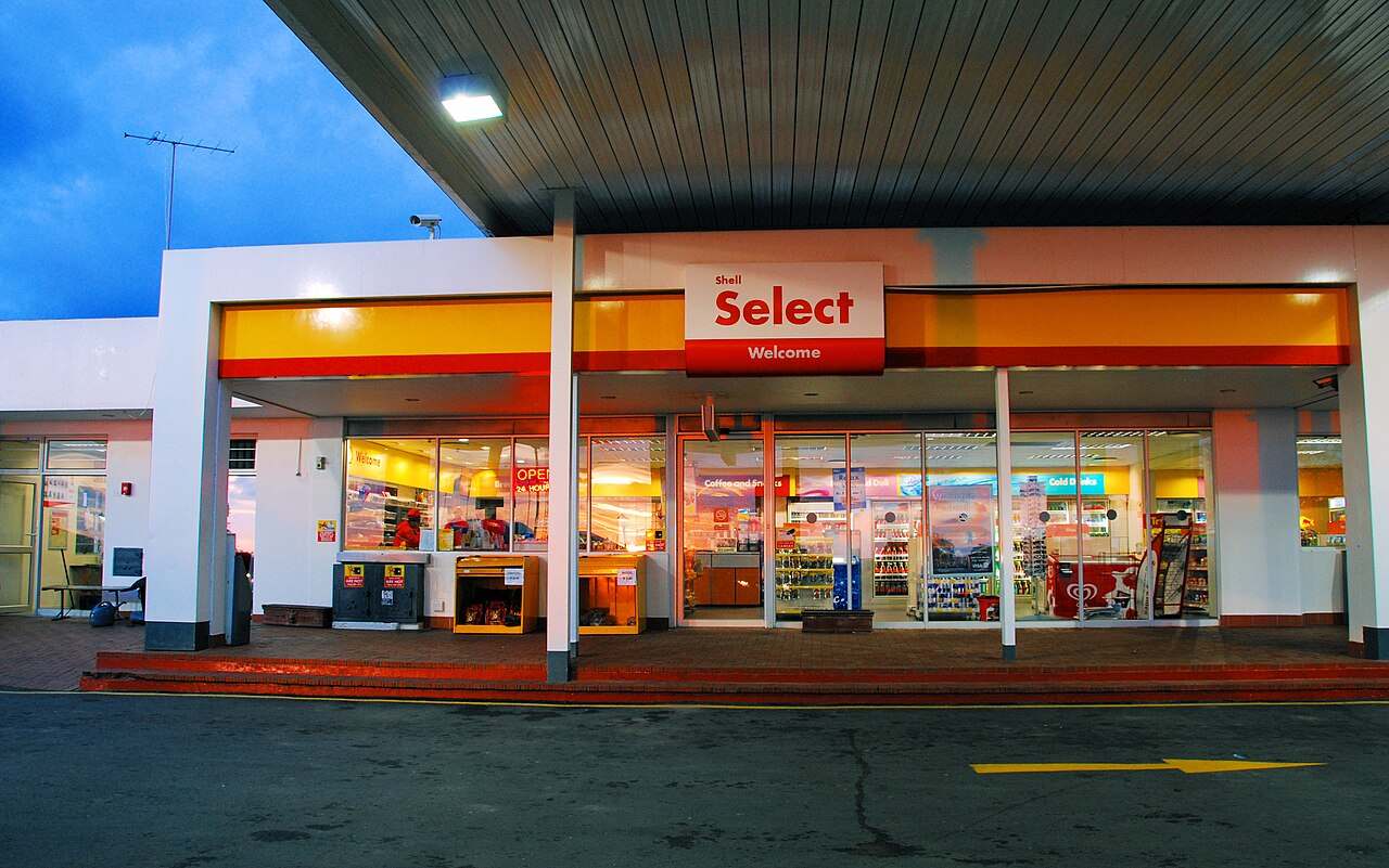 Lit Shell Select convenience shop under a service station canopy at dusk