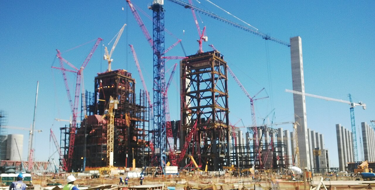 Cranes surround the steel frames of boiler units under construction at the Kusile coal power station in Mpumalanga, with workers in hard hats in the foreground