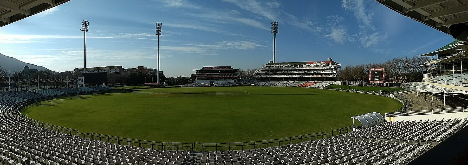 Panoramic view of the empty stands, floodlights and green outfield at Newlands Cricket Ground in Cape Town under a blue sky