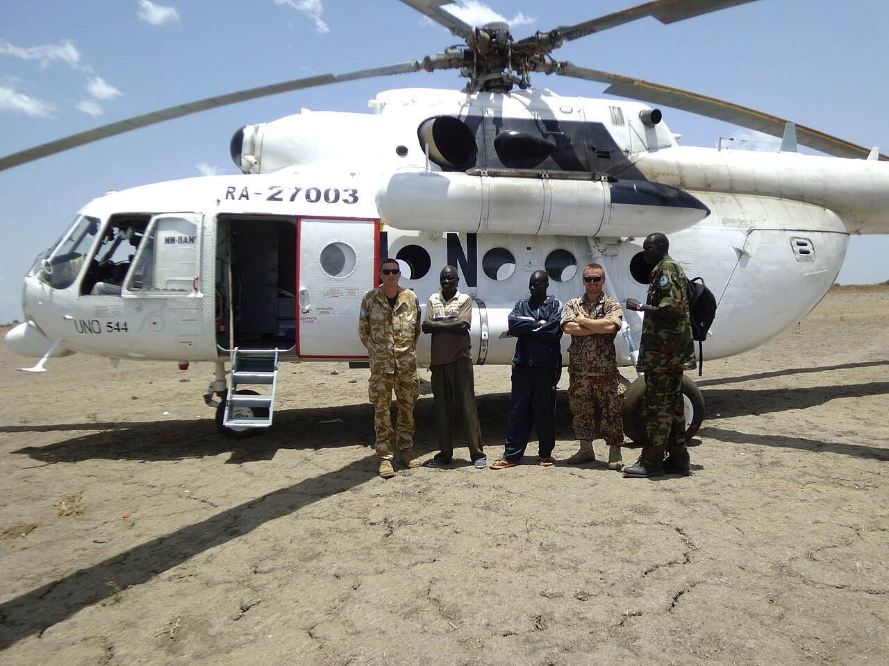 Five men stand in front of a white United Nations helicopter on dry cracked ground in South Sudan