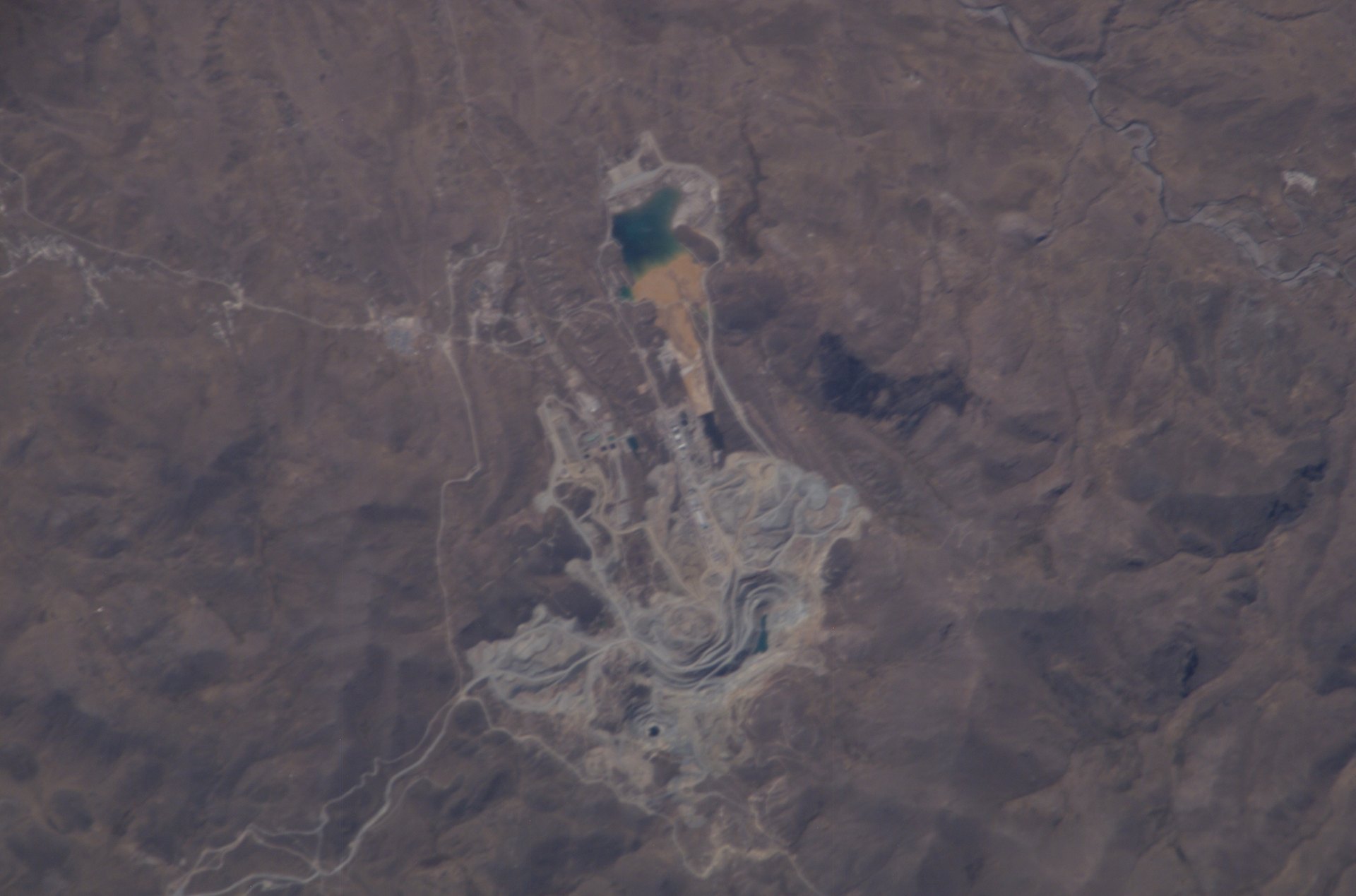 The Toquepala open-pit copper mine in the arid mountains of southern Peru seen from space, with its terraced pit, waste dumps and a reservoir