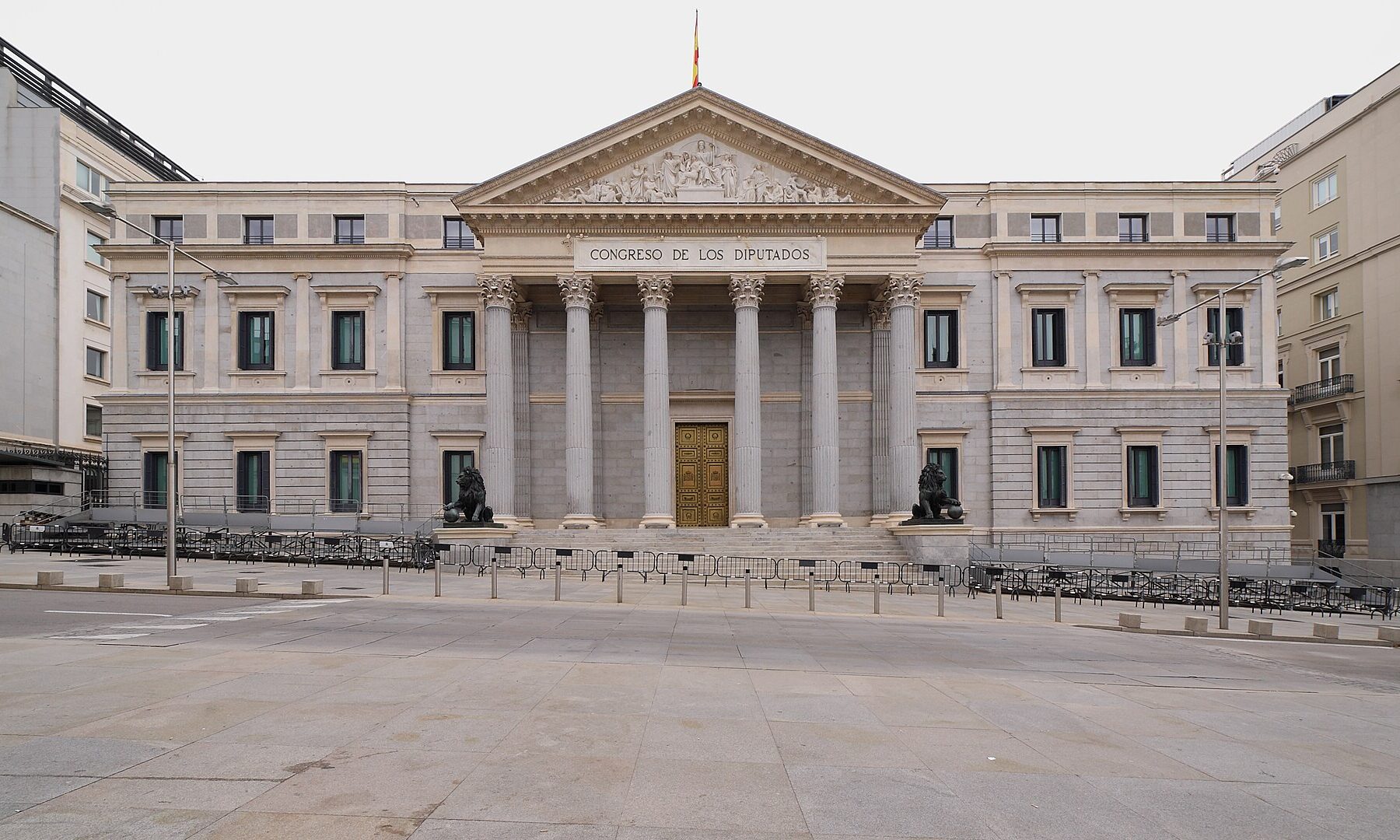 The neoclassical facade of Spain's Congress of Deputies in Madrid, with columns, bronze lions and a Spanish flag on the roof